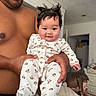 baby, child, person, adult, shirtless, indoor, bedroom, dog, animal, pajamas, floral_pattern, smiling, happy, hair, hands, face, furniture, doorway, blanket, skin