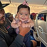 Kristyn is registered to the contest to win money with this photo: baby, child, man, airplane, interior, seat, smile, bow, clothing, person, holding, happy, transportation, casual, jeans, hat, beard, travel, portrait, family