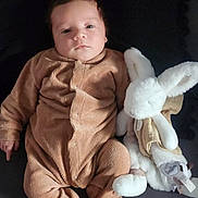 Ezio a rejoint le concours — aidez-le/la à gagner de superbes lots ! baby, infant, onesie, brown_clothing, stuffed_animal, bunny, soft_toy, lying_down, child, cute, indoors, portrait, young_child, cozy, sleepwear, plush, comfort, resting, adorable, face