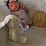 Kyomi is registered to the contest to win money with this photo: baby, infant, newborn, headband, pink_bow, floral_dress, plush_bunny, stuffed_animal, blanket, white_blanket, embroidery, decor, age_marker, 1_month, cute, portrait, lying_down, soft_toys, infant_clothing, baby_girl