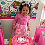 child, birthday_cake, hello_kitty, pink_dress, gift_bags, balloon, party, smile, curly_hair, celebration, number_2_candle, table, wall_decor, birthday, cake, person, indoors, colorful, happy, decorations