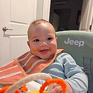 Sawyer is registered to the contest to win money with this photo: baby, smiling, bib, high_chair, toy, messy, indoor, child, happy, person, clothing, face, hand, furniture, room, door, seat, play, infant, cute