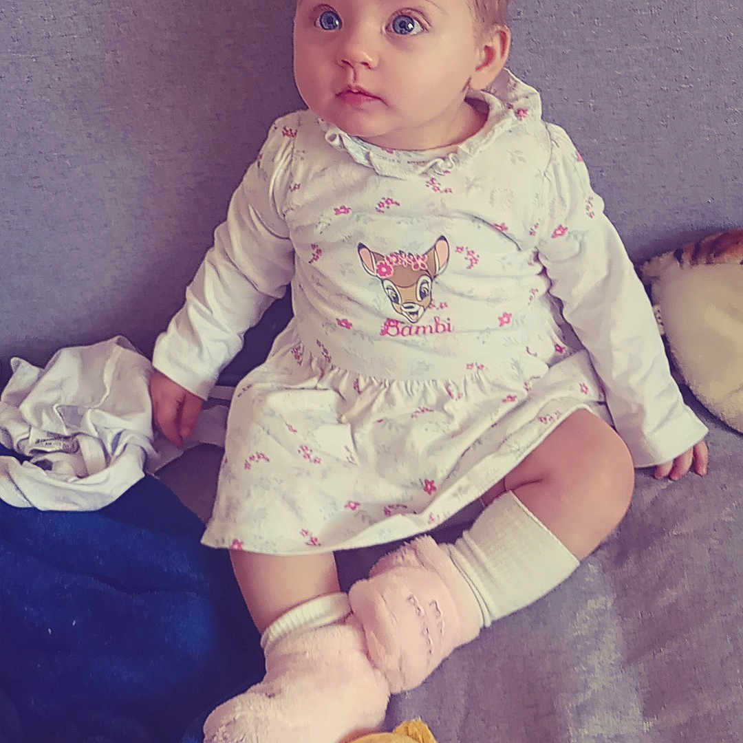 Ashley a rejoint le concours — aidez-le/la à gagner de superbes lots ! baby, child, girl, dress, floral, bambi, sitting, couch, blanket, plush_toy, winnie_the_pooh, pink_socks, white_socks, indoor, cute, portrait, soft_toys, furniture, curious, young_child