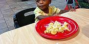 Charity is registered to the contest to win money with this photo: toddler, child, indoor, restaurant, food, pasta, pizza, plate, table, chair, person, hair, curious, casual, dining, floor, cabinet, colorful, meal, seated