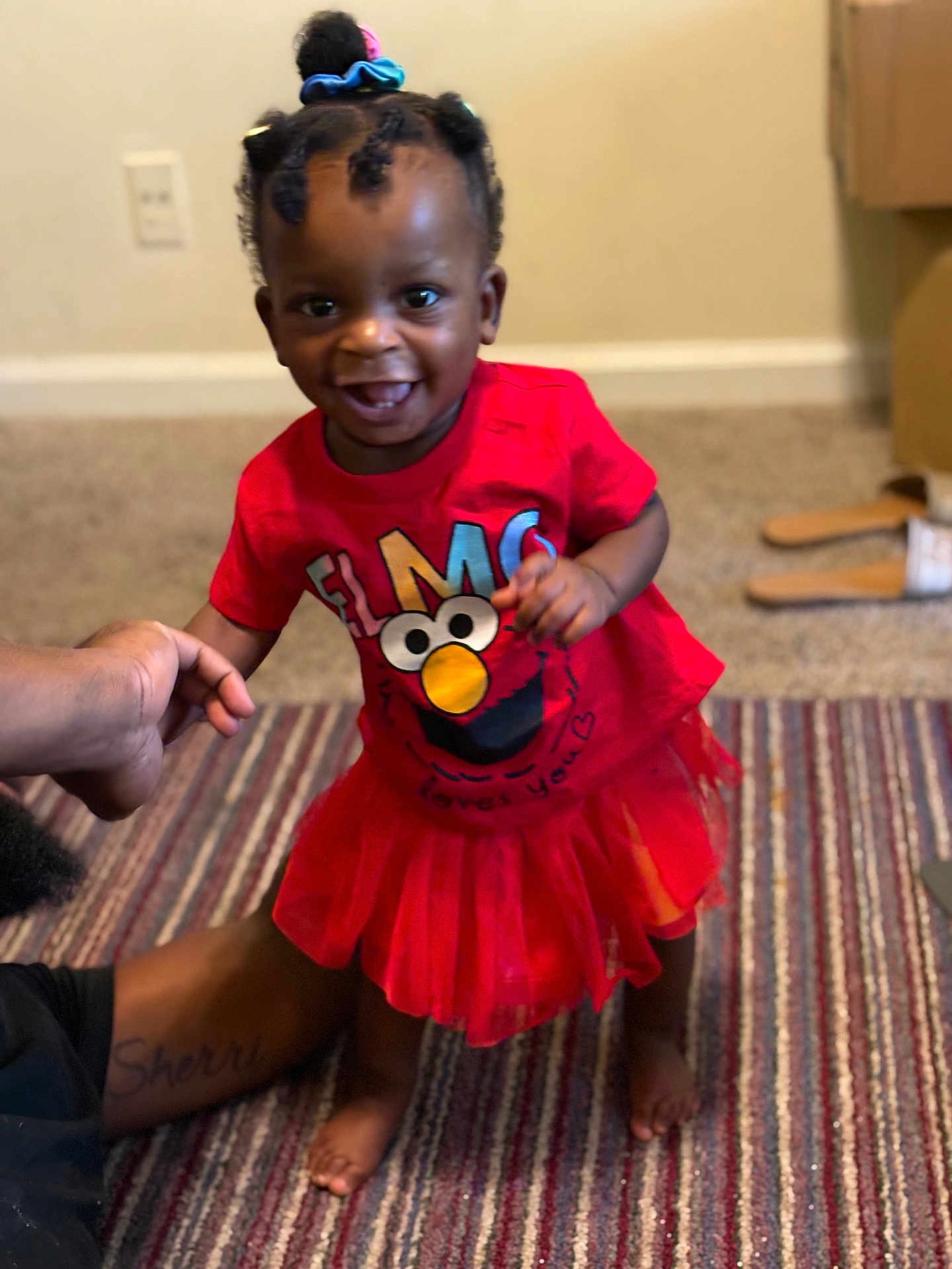 Charity joined the competition — help win amazing prizes! toddler, child, smiling, indoor, carpet, red_clothing, elmo, tshirt, tutu_skirt, barefoot, hair_accessories, person, adult_hand, home, floor, wall, toy, happy, cute, baby