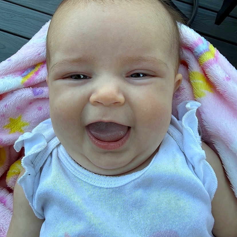 Gracie joined the competition — help win amazing prizes! baby, smiling, blanket, white_clothing, outdoor, wooden_deck, happy, face, infant, cute, person, closeup, child, sleeveless, toddler, expression, young, skin, head, portrait