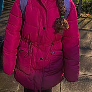 Alicia participe au concours pour gagner de l'argent avec cette photo : child, girl, pink_jacket, braid, boots, backpack, outdoor, sunlight, pavement, festive_hat, lights, smile, face, winter_clothing, fence, greenery, standing, portrait, holiday, casual