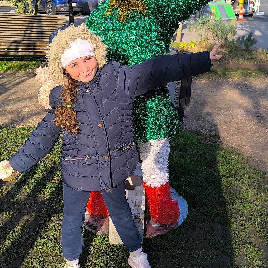 Alicia participe au concours pour gagner de l'argent avec cette photo : blue_sky, child, daylight, footwear, grass, hat, holiday, jacket, outdoor, park, person, playful, pose, santa_hat, sidewalk, smiling, statue, sunlight, tree, winter_clothing