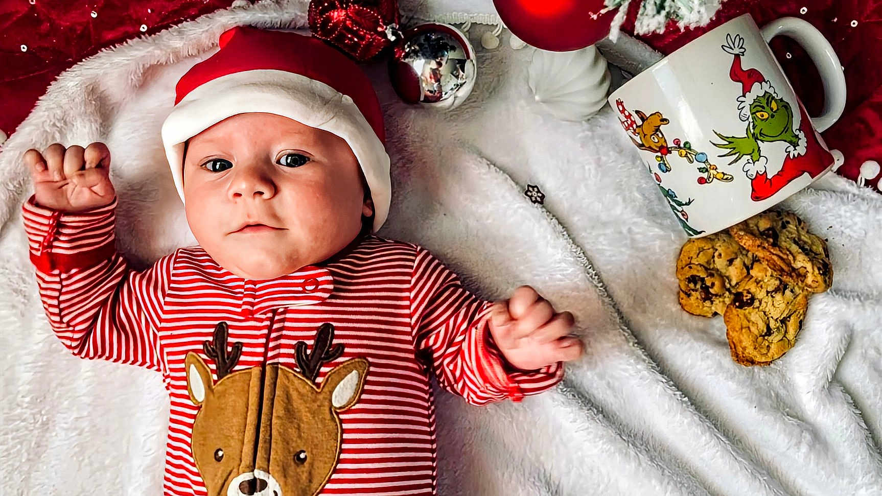Braxton is registered to the contest to win money with this photo: baby, infant, christmas, holiday, santa_hat, reindeer, striped_clothing, blanket, cookies, mug, grinch, festive, red, white, cute, smiling, indoors, celebration, child, face