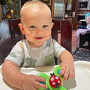 Camden joined the competition — help win amazing prizes! toddler, child, high_chair, toy, ladybug, smiling, indoor, kitchen, wooden_chair, clothing, short_sleeve, face, hands, playing, cute, happy, person, furniture, home, light