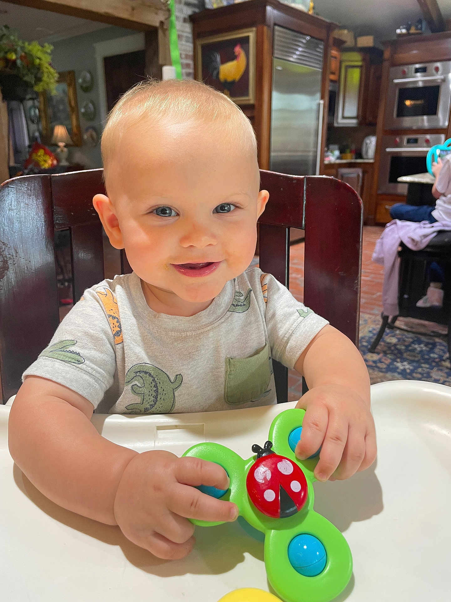 Camden joined the competition — help win amazing prizes! toddler, child, high_chair, toy, ladybug, smiling, indoor, kitchen, wooden_chair, clothing, short_sleeve, face, hands, playing, cute, happy, person, furniture, home, light