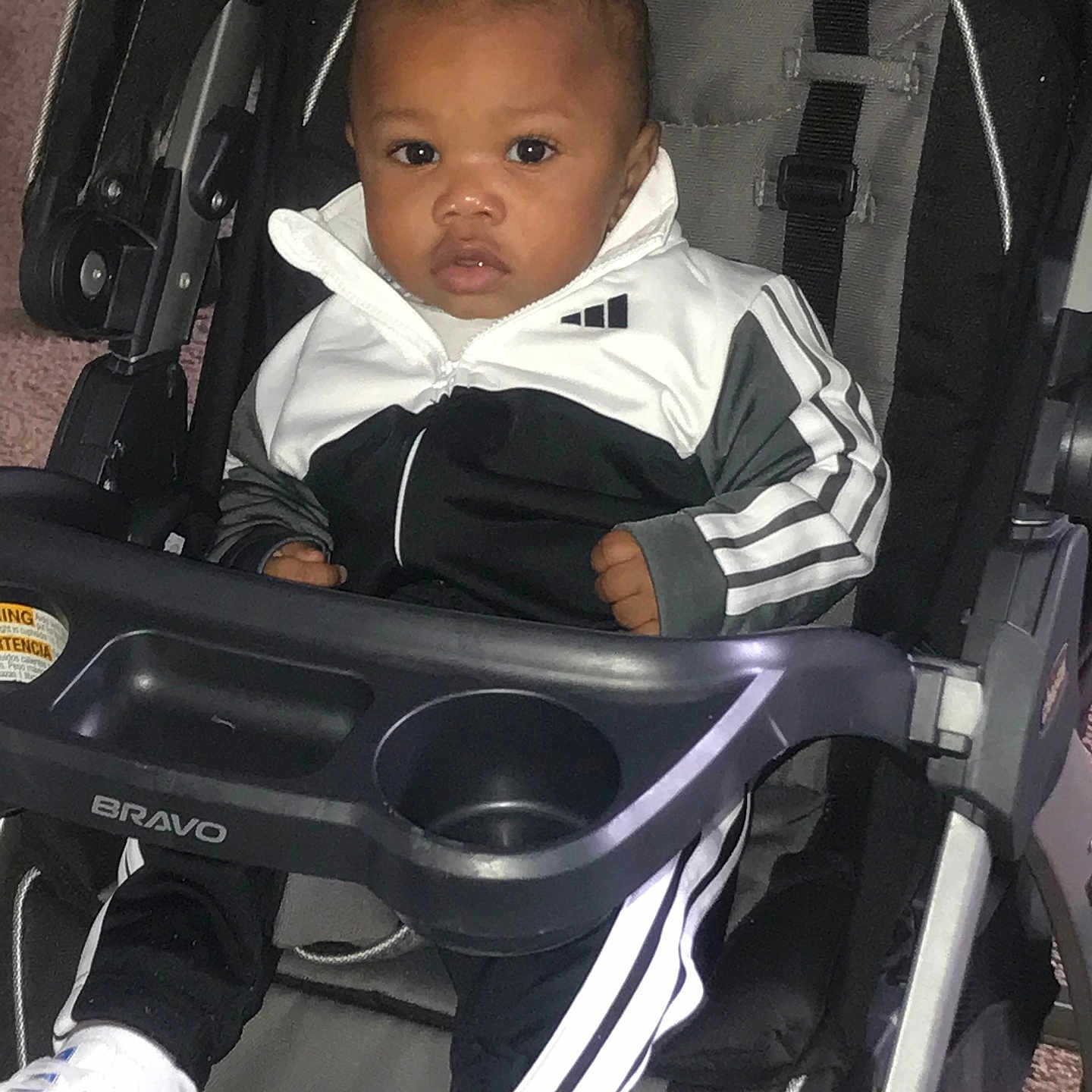 Kyshaun is registered to the contest to win money with this photo: baby, black, bravo, carpet, chicco, child, cute, expression, footwear, indoor, person, portrait, seat, shoes, sitting, sportswear, stroller, tracksuit, white, young_child