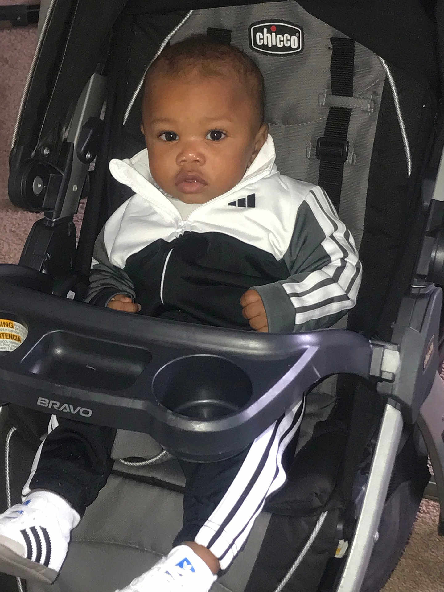 Kyshaun is registered to the contest to win money with this photo: baby, child, stroller, chicco, bravo, tracksuit, sportswear, shoes, white, black, sitting, indoor, carpet, footwear, person, portrait, young_child, cute, expression, seat