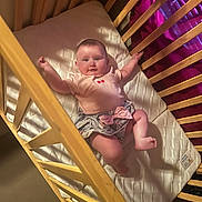 Peyton is registered to the contest to win money with this photo: baby, child, infant, crib, nursery, bedding, blanket, pillow, lying_down, smiling, happy, face, portrait, arms_raised, barefoot, pink_clothing, wooden_slats, indoor, cozy, photography