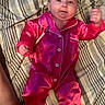Peyton joined the competition — help win amazing prizes! baby, child, infant, portrait, smiling, lying_down, pink_outfit, satin_clothing, pajamas, raised_fist, bed, bedding, striped_background, face, eyes, hands, indoor, cute, photography, newborn