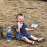 child, toddler, baby, sitting, smiling, outdoor, sand, dirt, rocks, trees, nature, dress, polka_dot, shoes, water_bottle, pointing, playground, adventure, portrait, sunlight