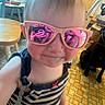 child, toddler, portrait, sunglasses, pink_glasses, striped_clothing, fashion, selfie, close_up, face, blond_hair, indoors, dog, pet, wooden_furniture, chair, table, carpet, reflection, smiling