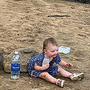 Cassidy is registered to the contest to win money with this photo: baby, child, toddler, outdoor, sandy_ground, woodland, rocks, bottle, water, dress, polka_dots, sitting, smiling, portrait, face, curious, shoes, nature, adventure, daylight