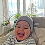 baby, blanket, child, cozy, curtains, expression, furniture, happy, hat, headwear, high_chair, home, indoor, laughing, natural_light, person, plants, smile, striped_shirt, young_child