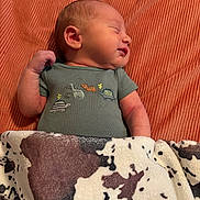 Bailey is registered to the contest to win money with this photo: newborn, baby, sleeping, blanket, cow_print, onesie, dinosaur_embroidery, orange_background, infant, cute, peaceful, child, portrait, soft_texture, cozy, indoors, resting, small_person, wrapped, warm