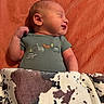 newborn, baby, sleeping, blanket, cow_print, onesie, dinosaur_embroidery, orange_background, infant, cute, peaceful, child, portrait, soft_texture, cozy, indoors, resting, small_person, wrapped, warm
