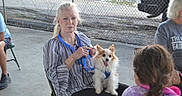 Olleeoscar is registered to the contest to win money with this photo: blue_lanyard, casual, chain_link_fence, chair, concrete_floor, conversation, daylight, dog, elderly_woman, event, fluffy_dog, grey_hair, happy_dog, leash, outdoor, park, people, sitting, small_dog, tie_dye_shirt