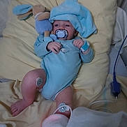 Mayron a rejoint le concours — aidez-le/la à gagner de superbes lots ! baby, pacifier, plush_toy, blue_onesie, blue_hat, pillow, medical_sensor, hospital, infant, bed, blanket, monitoring_device, soft_toys, lying_down, cute, child, person, healthcare, resting, indoors