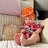 Wrenley is registered to the contest to win money with this photo: baby, infant, child, headband, bow, colorful_clothing, couch, blanket, milestone_sign, flower_decor, indoors, portrait, sitting, cute, soft_texture, focus, foot, skin, expression, decor