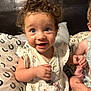 toddler, child, curly_hair, blue_eyes, smiling, bed, pillow, floral_dress, pacifier_clip, indoor, person, cute, happy, sitting, skin, hand, face, infant, candid, young_child