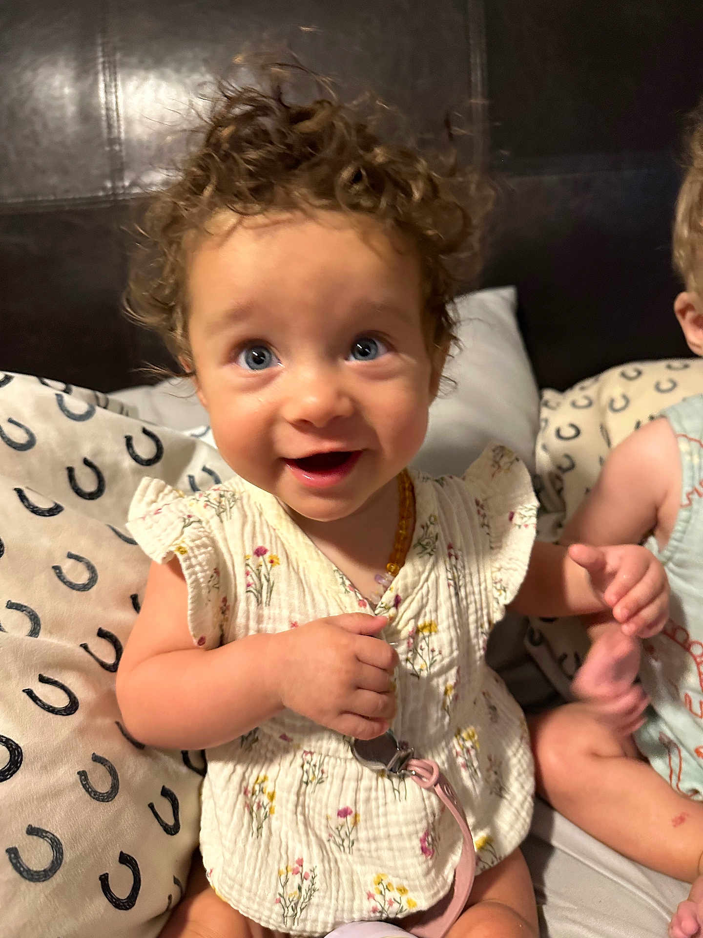 Wrenley joined the competition — help win amazing prizes! toddler, child, curly_hair, blue_eyes, smiling, bed, pillow, floral_dress, pacifier_clip, indoor, person, cute, happy, sitting, skin, hand, face, infant, candid, young_child