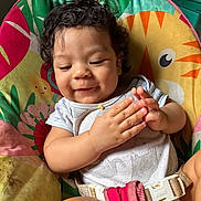 Azariah is registered to the contest to win money with this photo: baby, child, curly_hair, smiling, clapping_hands, baby_seat, colorful, animal_prints, comfort, happy, infant, cute, casual_clothing, indoor, playful, seat_belt, soft_lighting, close_up, portrait, toddler