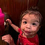 toddler, child, face, hands, food, sippy_cup, table, wood_paneling, red_shirt, curly_hair, indoor, closeup, expression, messy, cute, portrait, person, young_child, sitting, eye_contact