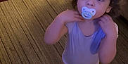Amari is registered to the contest to win money with this photo: toddler, child, pacifier, curly_hair, barefoot, onesie, carpet, indoor, bed, rug, floor, person, looking_up, standing, home, curious, young_child, baby, furniture, soft_lighting