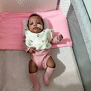 Janiyah joined the competition — help win amazing prizes! baby, infant, crib, blanket, pillow, face, feeding_tube, clothing, pink, socks, person, bed, soft_texture, cute, lying_down, indoors, child, baby_bib, healthcare, newborn