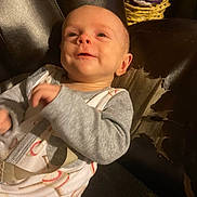 Sawyer is registered to the contest to win money with this photo: baby, child, smile, pajamas, baseball_print, face, leather_chair, worn_out, indoor, cozy, person, infant, cute, happy, sitting, clothing, background, fabric, seat, relax