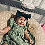 baby, infant, smile, green_dress, headband, bow, cushion, wooden_sign, four_months, playpen, baby_accessories, patterned_fabric, lying_down, happy, child, indoors, milestone, cute, person, portrait