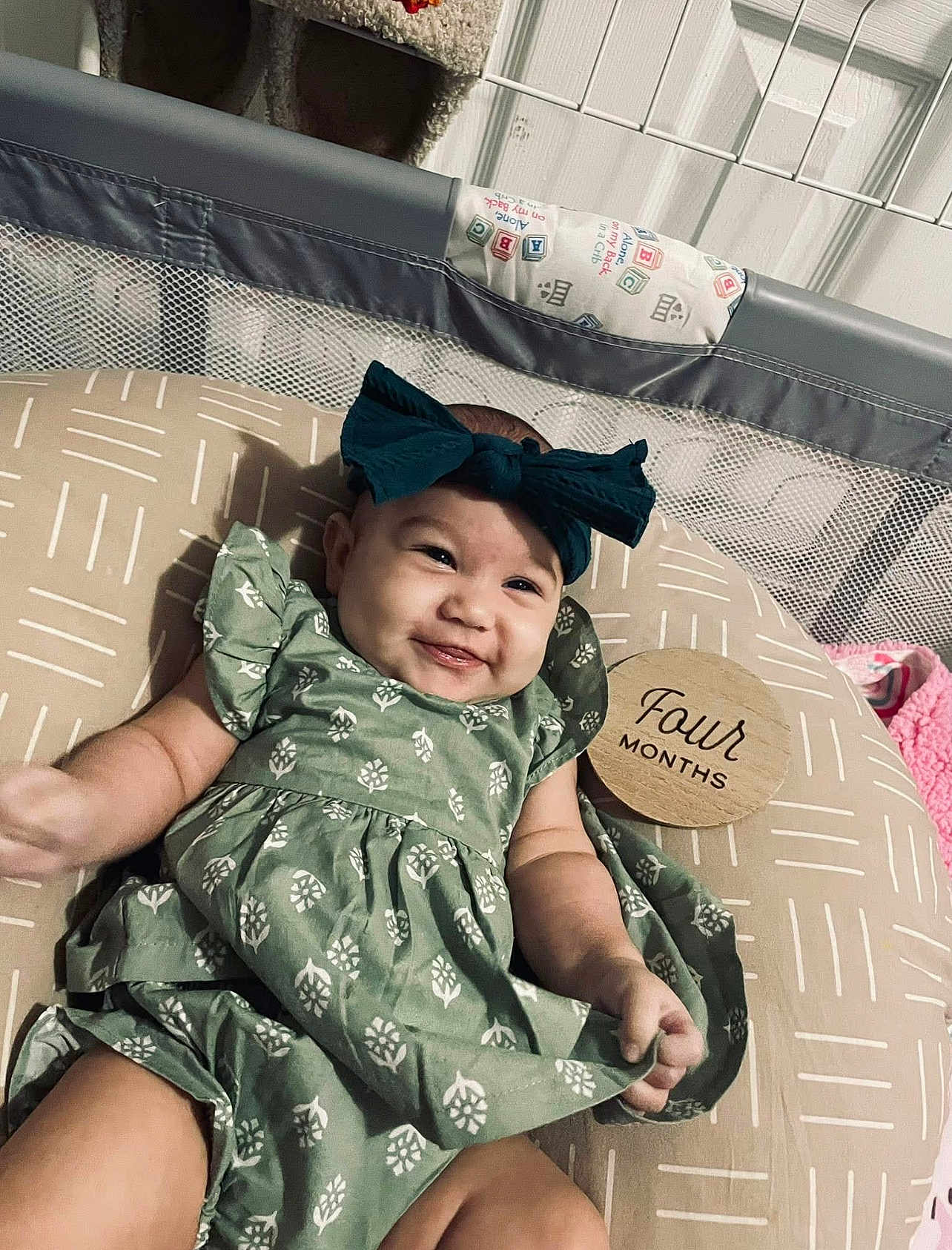 Hadley joined the competition — help win amazing prizes! baby, infant, smile, green_dress, headband, bow, cushion, wooden_sign, four_months, playpen, baby_accessories, patterned_fabric, lying_down, happy, child, indoors, milestone, cute, person, portrait