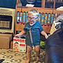 toddler, child, glasses, blue_shirt, barefoot, indoor, crib, cardboard_box, floor_tile, furniture, living_room, toy, clutter, person, movement, home, couch, box, diaper_box, floor