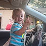Kohen joined the competition — help win amazing prizes! toddler, child, car_interior, steering_wheel, person, hand, window, adult, clothing, seat, dashboard, rhinestones, blurred_background, curious_expression, inside_vehicle, daylight, hand_holding, vehicle, seatbelt, people_outside