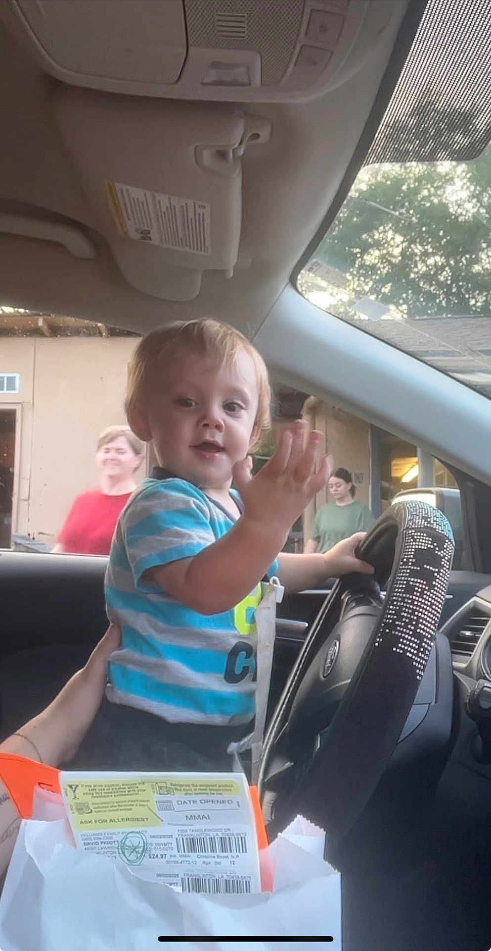 Kohen joined the competition — help win amazing prizes! toddler, child, car_interior, steering_wheel, person, hand, window, adult, clothing, seat, dashboard, rhinestones, blurred_background, curious_expression, inside_vehicle, daylight, hand_holding, vehicle, seatbelt, people_outside