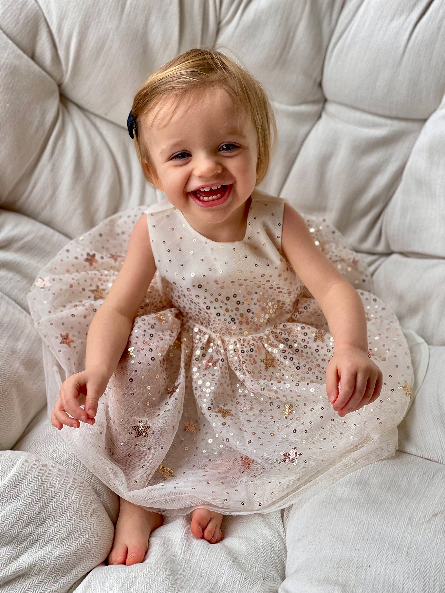 Mathilde participe au concours pour gagner de l'argent avec cette photo : baby_toddler_clothing, blond, child, comfort, couch, dress, eye, facial_expression, finger, hand, happy, human, iris, joy, living_room, mouth, nose, person, sitting, skin