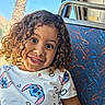 blue_sky, bus_seat, casual_clothing, child, curly_hair, cute, daylight, happy, indoors, palm_tree, patterned_fabric, person, portrait, public_transport, seat, smile, stitch_character, tshirt, window, young