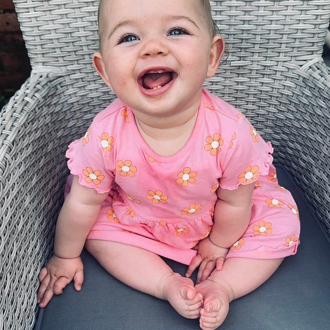 Willow is registered to the contest to win money with this photo: baby, bodypart, chair, clothing, cushion, dress, face, furniture, happy, head, homedecor, laughing, mouth, pants, person, photography, portrait, sitting, t_shirt, teeth