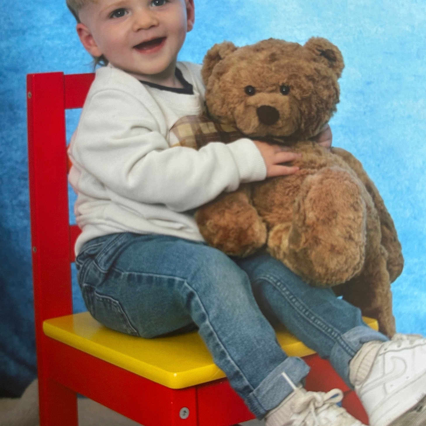Theo joined the competition — help win amazing prizes! blue_background, casual_clothing, child, cute, happy, indoor, jeans, person, plush_toy, portrait, red_chair, sitting, smiling, studio_photo, teddy_bear, toddler, toy, white_sneakers, white_sweatshirt, yellow_seat