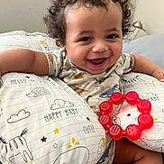 Zavian joined the competition — help win amazing prizes! baby, child, smiling, curly_hair, pillow, teething_ring, toy, bed, cute, happy, infant, indoor, clothing, person, face, arm, sitting, cute_animal_print, nursery, comfort