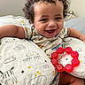 baby, child, smiling, curly_hair, pillow, teething_ring, toy, bed, cute, happy, infant, indoor, clothing, person, face, arm, sitting, cute_animal_print, nursery, comfort