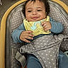 baby, smiling, bib, blue_clothing, curly_hair, baby_rocker, patterned_fabric, indoor, child, seat_belt, happy, infant, person, portrait, young_child, comfortable, cute, relaxed, furniture, closeup