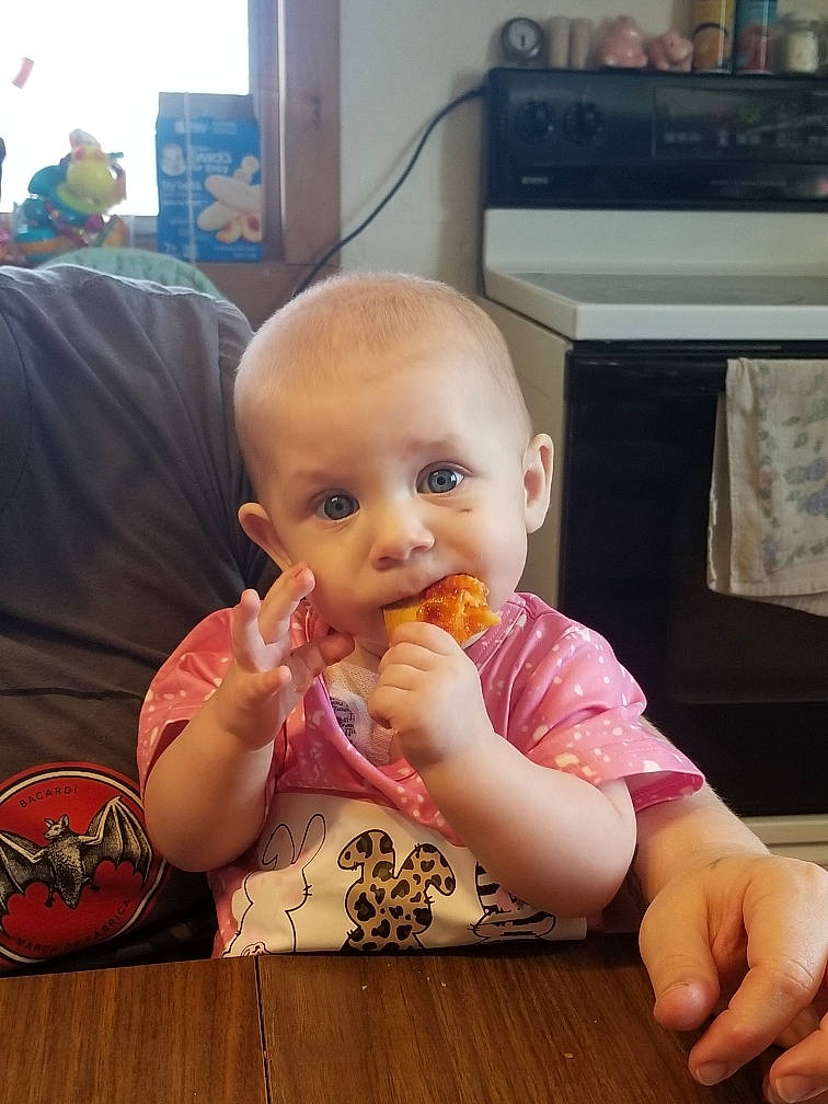 Lucille is registered to the contest to win money with this photo: baby, baby_toddler_clothing, chair, child, desk, eating, finger, flooring, food_craving, hand, home_appliance, person, room, sitting, skin, table, tableware, television, thumb, toddler