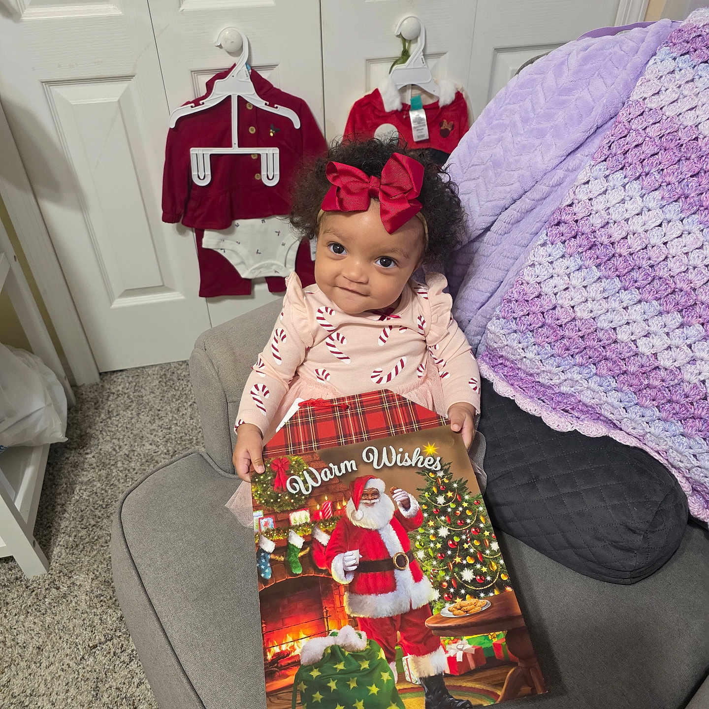 Omyah is registered to the contest to win money with this photo: blanket, carpet, child, christmas_book, clothing, couch, cozy, curly_hair, door, festive, furniture, girl, hanger, holiday_outfits, indoor, portrait, red_bow, santa_claus, smiling, toddler