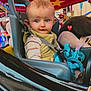 toddler, child, amusement_ride, seatbelt, plush_toy, blue_eyes, carnival, stars, ride_car, jacket, striped_shirt, indoor, colorful, face, expression, toy, seat, helmet, fun, entertainment